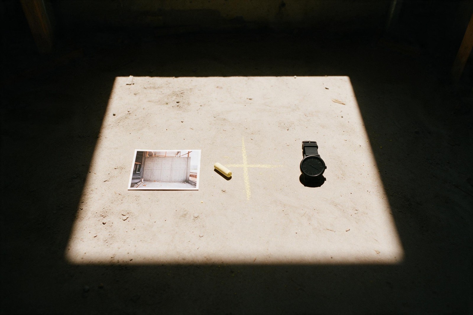 A photo, a chalk cross and a watch on a concrete floor